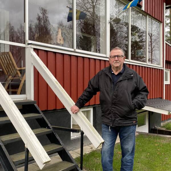 En man med glasögon står vid att trappa framför ett rött hus.