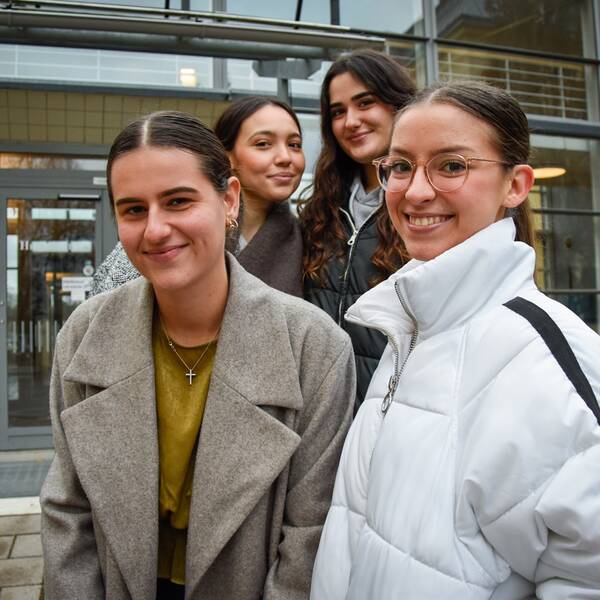 Fyra unga utlandsstudenter poserar fram Högskolan Gävles huvudingång i glas.