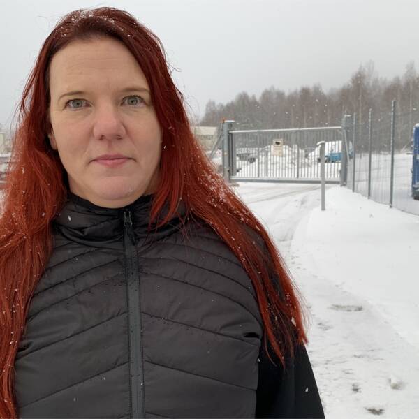 En kvinna med rött långt hår, har en svart täckjacka, står utomhus i snöväder. Hon heter Helena Andersson, ordförande för Postklubben i Dalarna.