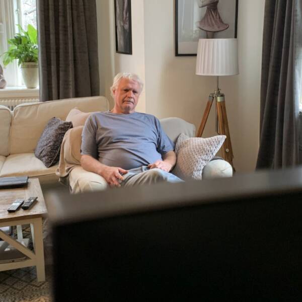 En äldre man sitter i en fåtölj och ser på tv.