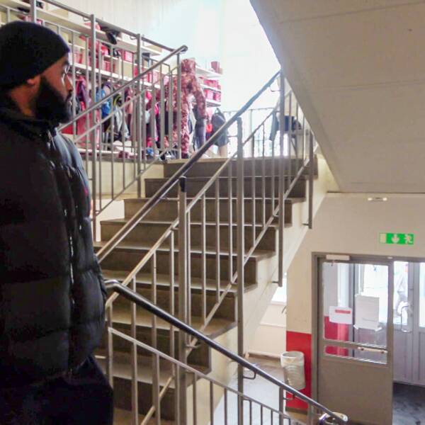 Abdirahman Mohammed, trygghetsvärd på Ryaskolan i Göteborg går ner för en trappa inne på skolan. Han tittar mot ytterdörrren.