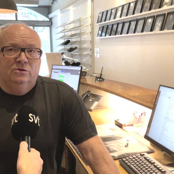Man med svart T-shirt och glasögon står bredvid en dator.