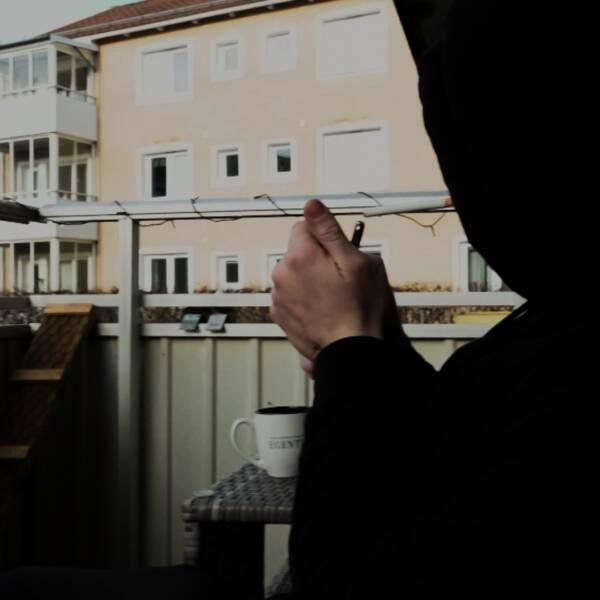 En man i luvtröja sitter på en balkong och tänker en cigarett