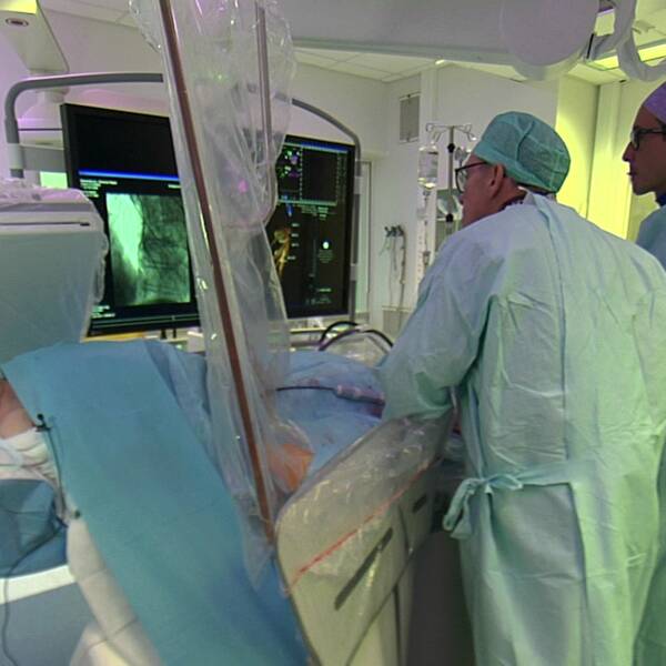 En kvinna ligger på ett operationsbord, tre vårdpersonal står över henne och kollar på en skärm