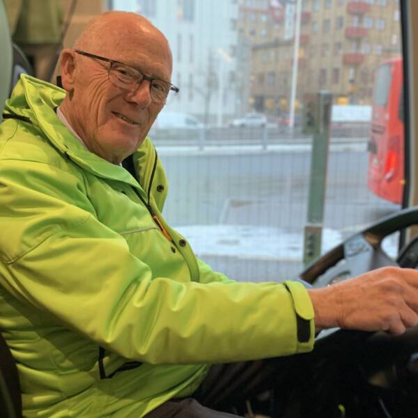 Erik Alm sitter i chaufförsstolen i bussen och håller i ratten. Han kollar in i kameran och ler.