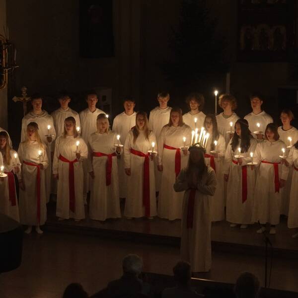 En luciakör står i en mörk kyrka med levande ljus.