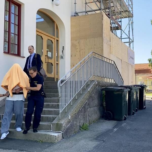 En man vars ansikte täcks av en filt leds ner för en trappa av vakter.
