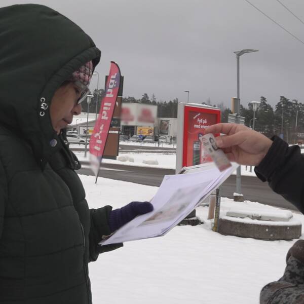 Kvinna med luva håller ett papper i handen i vintervitt landskap