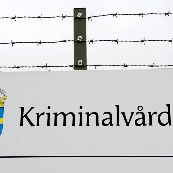 Exteriörbild på ett staket med Kriminalvårdens skylt.