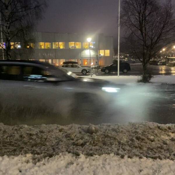 På bilden syns en bil som kör i vatten så att det skvätter upp. Framför bilen syns även en snöhög.