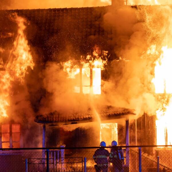 Övertänt hus med två brandmän i förgrunden