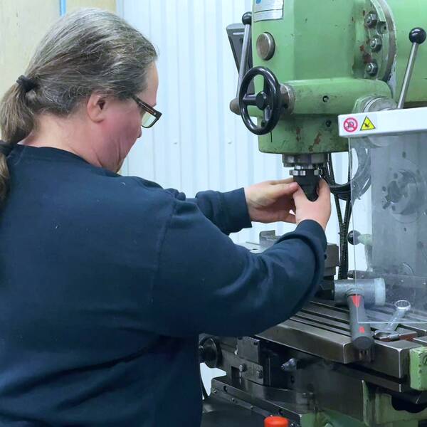 en medelålders kvinna arbetar vid en fräsmaskin i verkstad