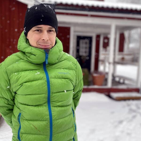 Sjuksköterskan Henrik Karlsson i Leksand står framför sitt röda hus med vita knutar. Det snöar och är vinter.