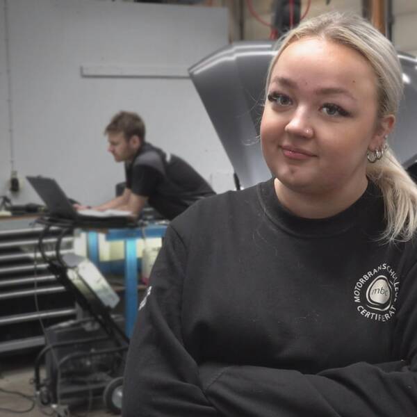 På bilden syns Julia som står till höger i bild. Hon har armarna i kors och tittar in i kameran. I bakgrunden syns en bil.
