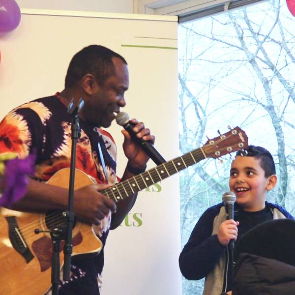 En man som håller i en gitarr och en mikrofon, bredvid honom står en ung kille med en mikrofon i handen.