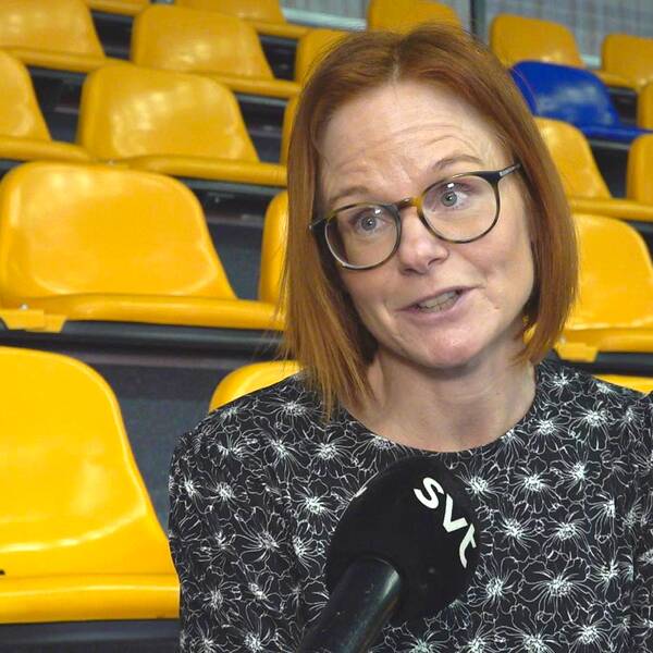 Camilla Olsson, kanslichef på Värmlands innebandyförbund, blir intervjuad när hon sitter på en läktare med gula och blå stolar i en sporthall.