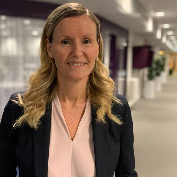 Linda Larsson, avdelningschef vid individ- och familjeomsorgen i Skellefteå kommun, står  i ett öppet kontorslandskap. Hon har lockat långt blont hår och här klädd i en puderrosa blus med en svart kavaj över.