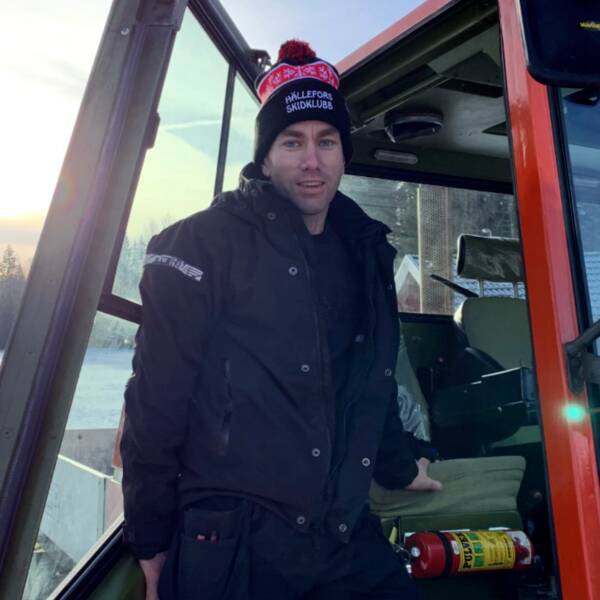 En man (Ordförande i skidklubben Hällefors SK Johan Ånger) står i dörren på en traktor/pistmaskin. Han är klädd i vinterkläder och det är soligt och snöigt bakom honom