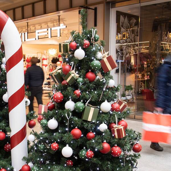 Julhandel i en galleria. En person går med kassar framför julgranar.