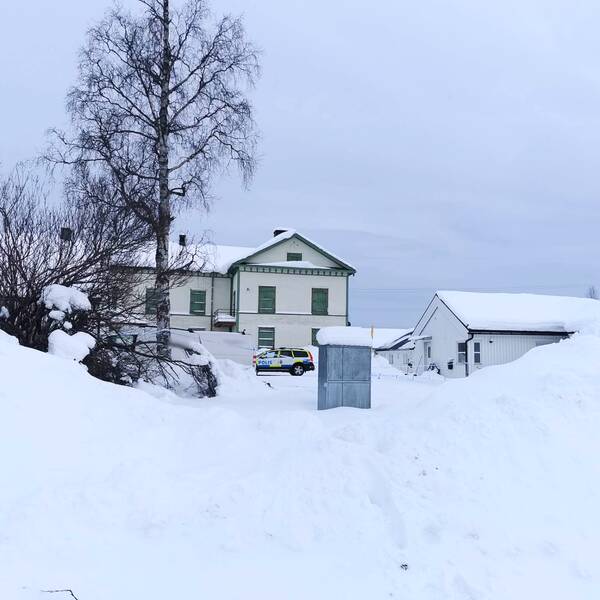 Vitt hus med gröna knutan och fönster i Gällivare. Framför huset syns en polisbil. Det är mycket snö. I förgrunden syns en björk och en snötäckt buske.