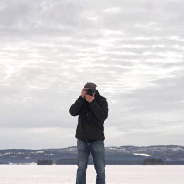 En man står i ett snölandskap och fotograferar med en kamera.