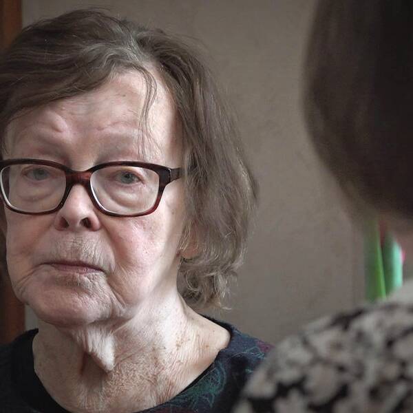 Äldre kvinna med glasögon och mörkt hår tittar uppgivet in i kameran.