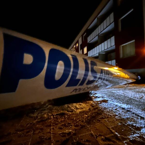 Ett flerfamiljshus i Ludvika en mörk februarikväll. Ett vitt polisband syns i förgrunden och sträcker sig från vänster i bild fram mot porten på lägenhetshuset.