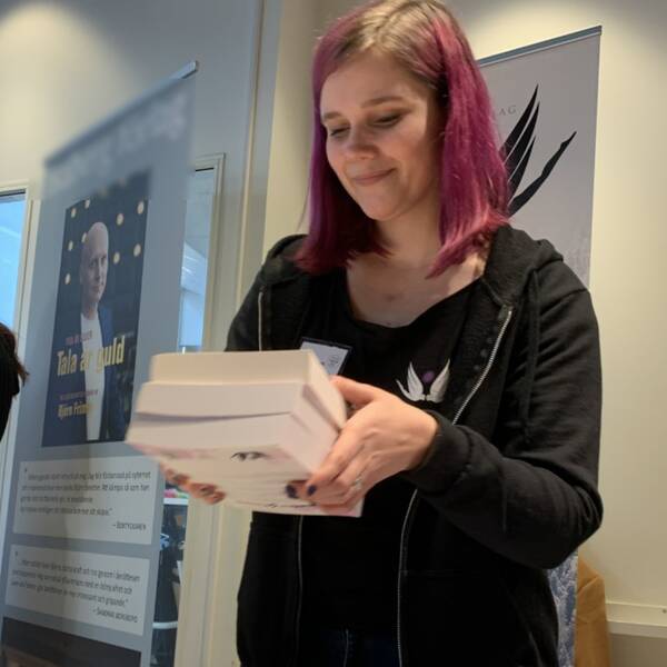 Gabriella Kjeilen lägger ner en trave böcker på ett bord. Hon ställer ut på Smålit 2023.