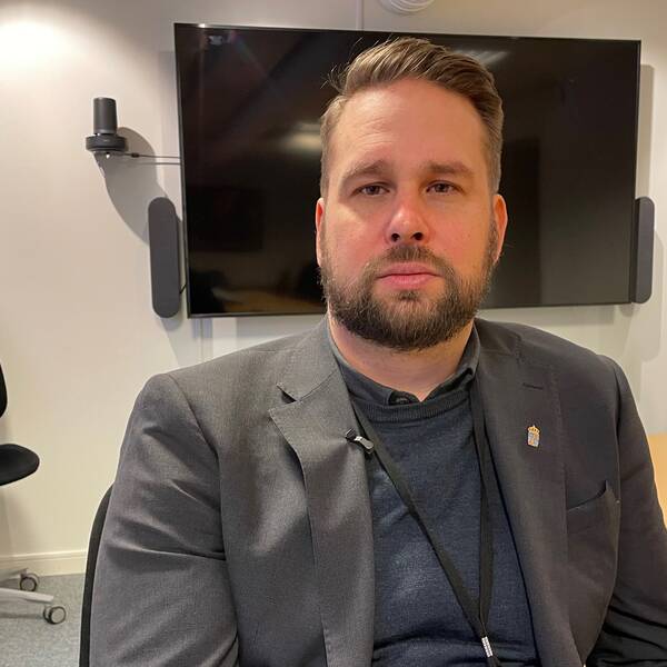 David Ström sitter i ett mötesrum framför en tv. Omkring sig har han ett par stolar. 