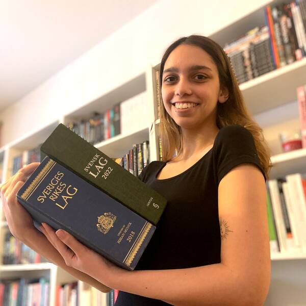 Mathilda Bandarian, tidigare den yngsta juriststudenten på juridiska institutionen, har tagit examen och håller upp två av Sveriges lagböcker.