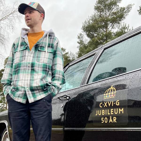 Philip Aronsson står på sin gård hemma i Jönköping framför sin Cadillac som har ett tryck där det står C XVI G jubileum 50 år på. Han står med båda händerna i fickan och kollar snett ut.