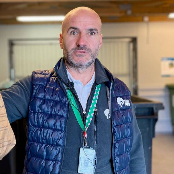 Hasan Berisha, kvartersansvarig på Helsingborgshem, tittar in i kameran. Han håller en matavfallspåse i handen och står i ett soprum. Sopor, återvinning, Helsingborgshem, så gör du för att återvinna rätt. Matavfall, grovsopor.