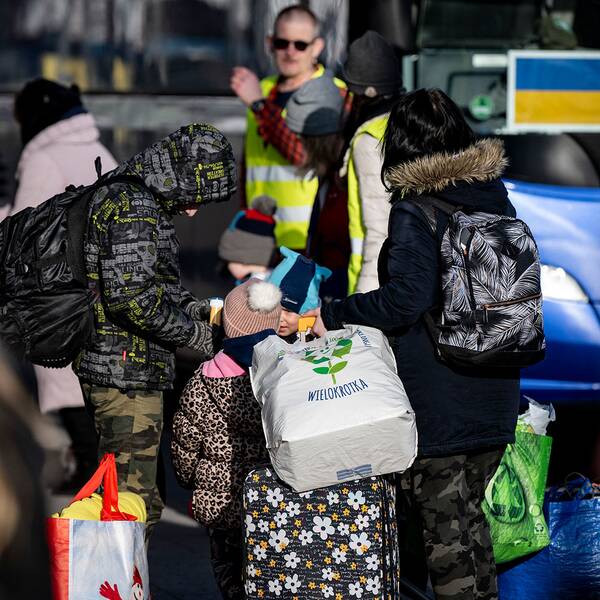 Människor som flytt från Ukraina står vid en buss i Karlskrona, en ukrainsk och en svensk flagga syns i fönstret på bussen. 