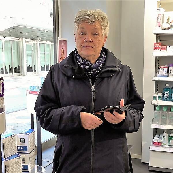 En äldre kvinna i ett apotek och med en mobiltelefon i handen.