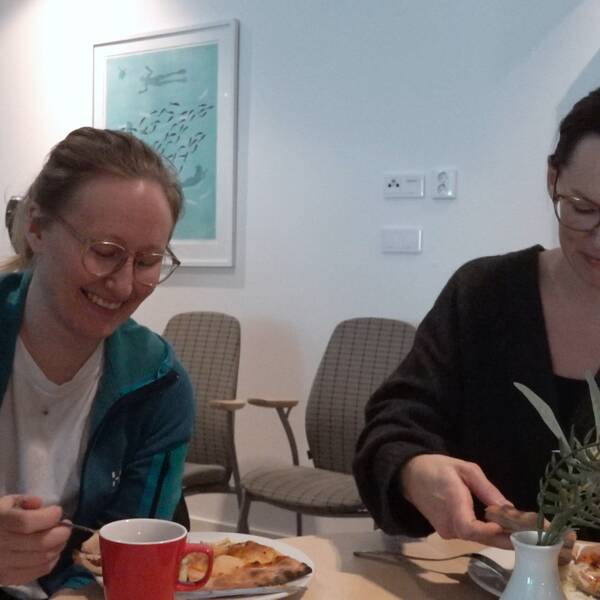 Två kvinnor sitter och äter pizza och är glada