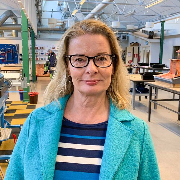 En bild på utbildningsministern Lotta Edholm som står inne i ett rum med plåtslagningsutrustning.