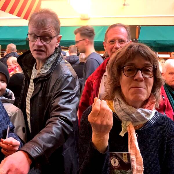 Människor står på en matfestival inomhus i Halmstad, pekar, provsmakar och tittar runt.