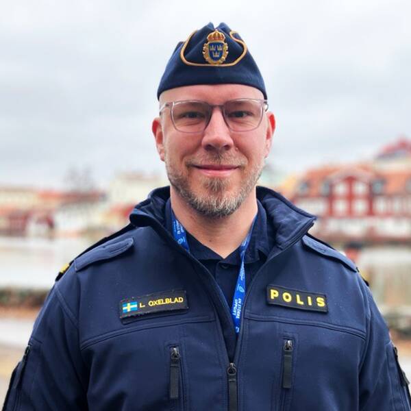 Bild på en manlig polis i uniform som står framför ett vattendrag och hus. Mannen heter Libbie Oxelblad och är Sörmlandspolisens attraherasamordnare. Han hoppas att distansutbildningen ska locka fler till polisyrket.