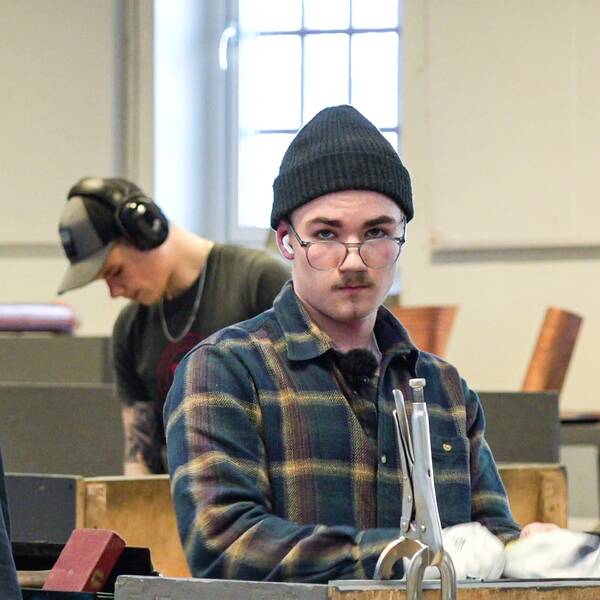 En kille i glasögon och mössa som heter Tor Lundström står vid en arbetsbänk. 