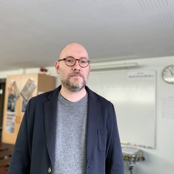 Kulturskolechefen Mikael Källarsson står i ett undervisningsrum med instrument framför en whiteboard.