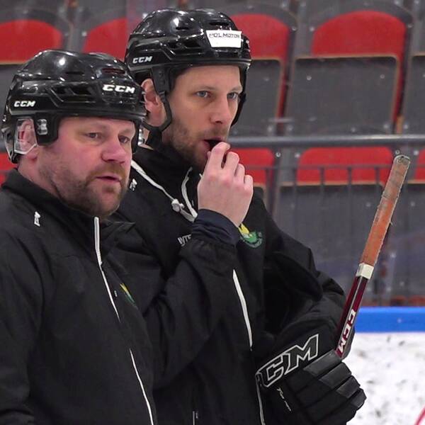 Kjell-Åke Andersson bredvid en annan man på en hockeyrink. De båda är klädda i svarta kläder och svarta hockeyhjälmar.