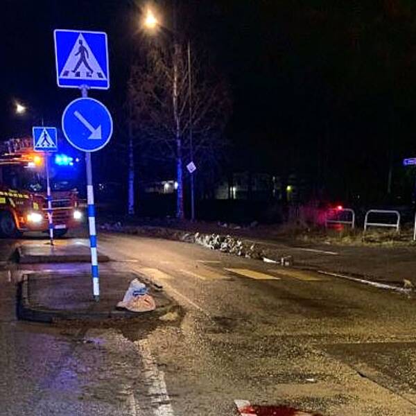 Bild på en gata med ett övergångsställe. Det är mörkt och man ser en brandbil i bakgrunden. I förgrunden syns lite av en brandman.