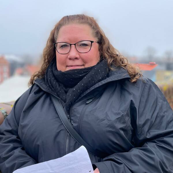 Feriesamordnare på Karlskrona kommun står lutad mot en vägg med en lista över sommarjobb i händerna.