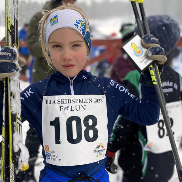 en ung flicka står med sina längdskidor och stavar i händerna i målområdet, det snöar