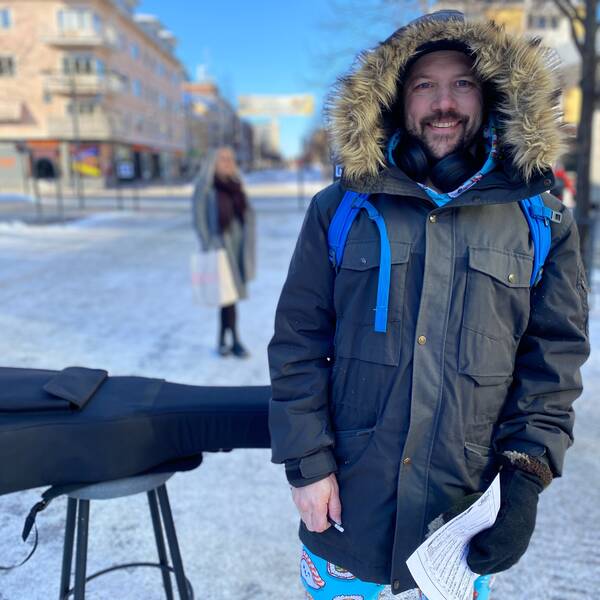 Anton Boström står iklädd vinterjacka med pälskrage och ler. Han har mörkt kort hår och skägg. Snett bakom honom längs gågatan i Luleå ligger gitarren på en pall.