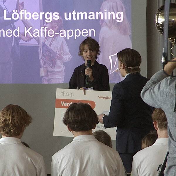 Ett barn står med en check, flera barn och unga är runt omkring