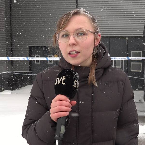 Bild på SVT:s reporter Serafia Olausson som håller i en SVT-mikrofon. Bakom henne syns polisavspärrningarna.
