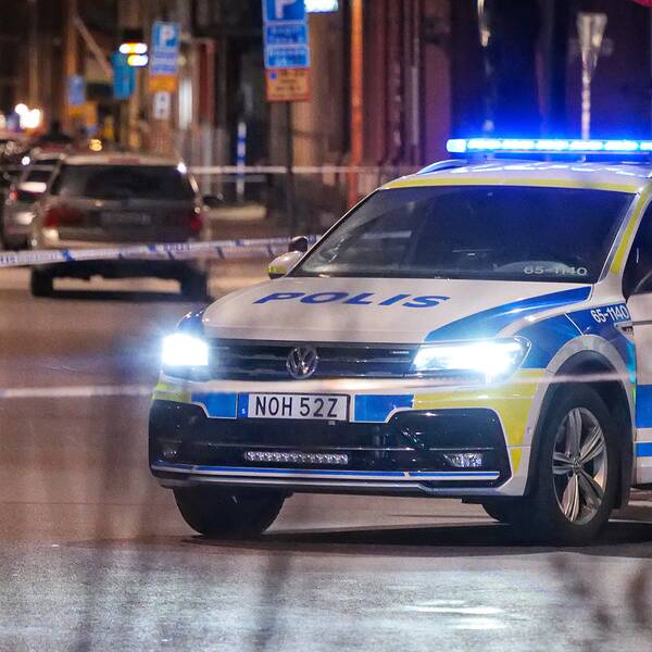 En bild på en polisbil som står innanför polisavspärrningar på en gata.