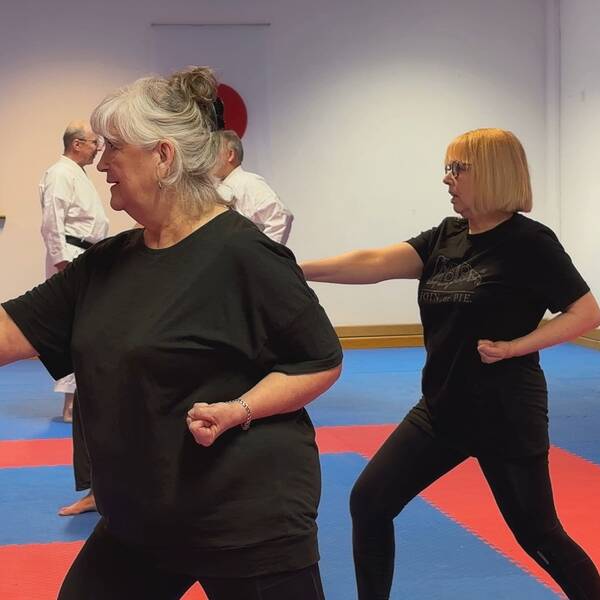 två kvinnor i pensionsålder som gör karate-rörelser på mattan i en dojo – en träningssal för kampsport