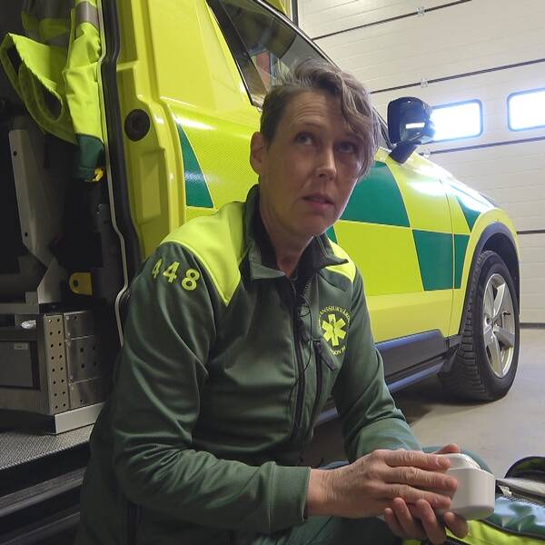 Ambulansvårdare sitter på huk vid en ambulans i ett garage.